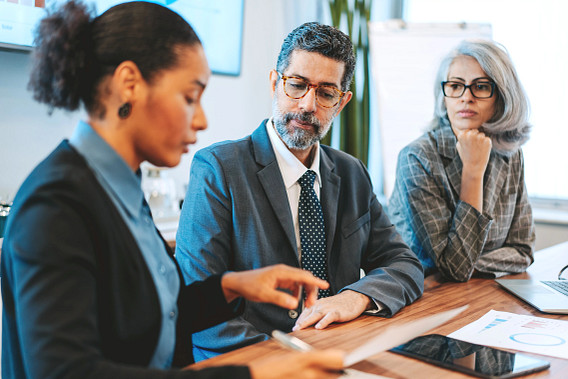 Three business people - two women and a man sitting at a desk, talking