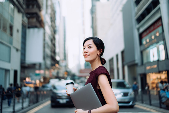 woma in street with coffee holding laptop underarm