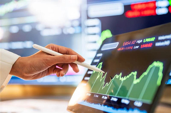 Close-up of a hand using a stylus to analyze financial trends on a digital tablet, showing fluctuating stock market graphs and data.
