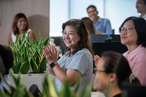 A smiling woman stood in the office with colleagues while clapping